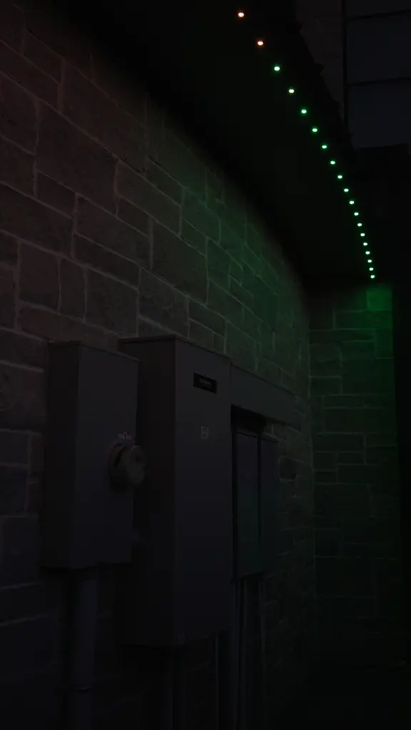 Permanent roofline lights set to green along the eave above a stone wall at night