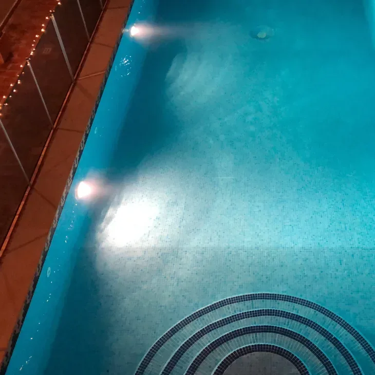 Two underwater pool lights glowing in a blue tiled pool at night