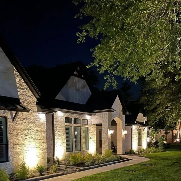 Stone home front lit at night by landscape uplights and entry lanterns