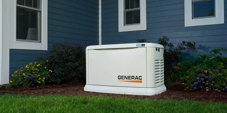 Generac standby generator in a garden bed by a blue house