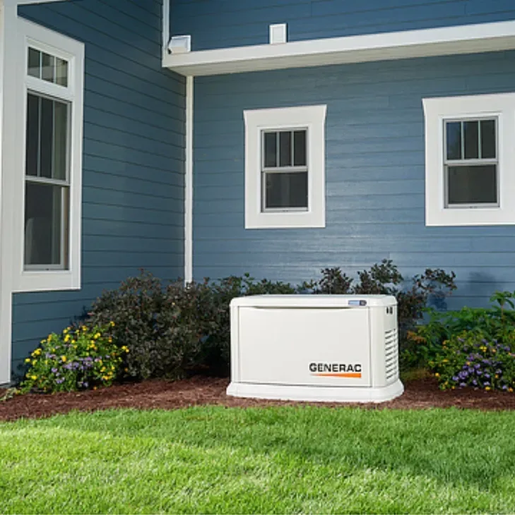 Generac home standby generator in a flower bed beside a blue house
