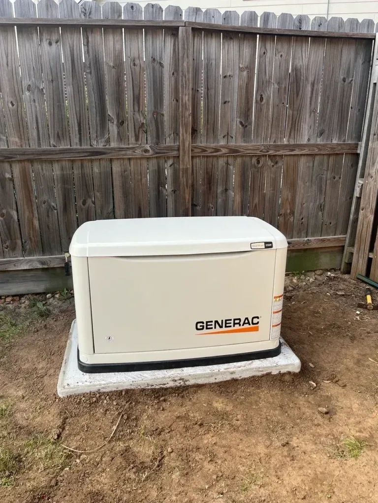 Generac Guardian standby generator on a pad beside a wooden fence