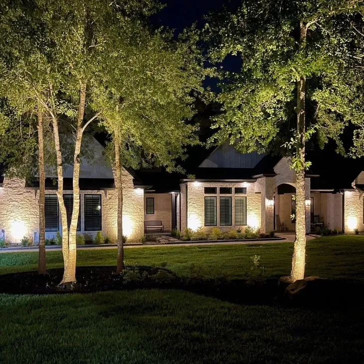 Stone home at night with landscape uplights on the walls and trees