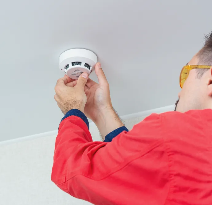 Technician installing a smoke detector on a ceiling